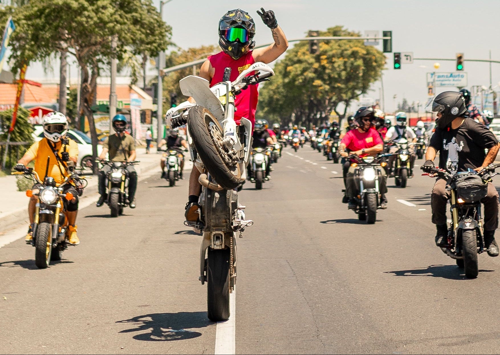 Motorcycle rider performing a stunt on a city street with other riders in the background.